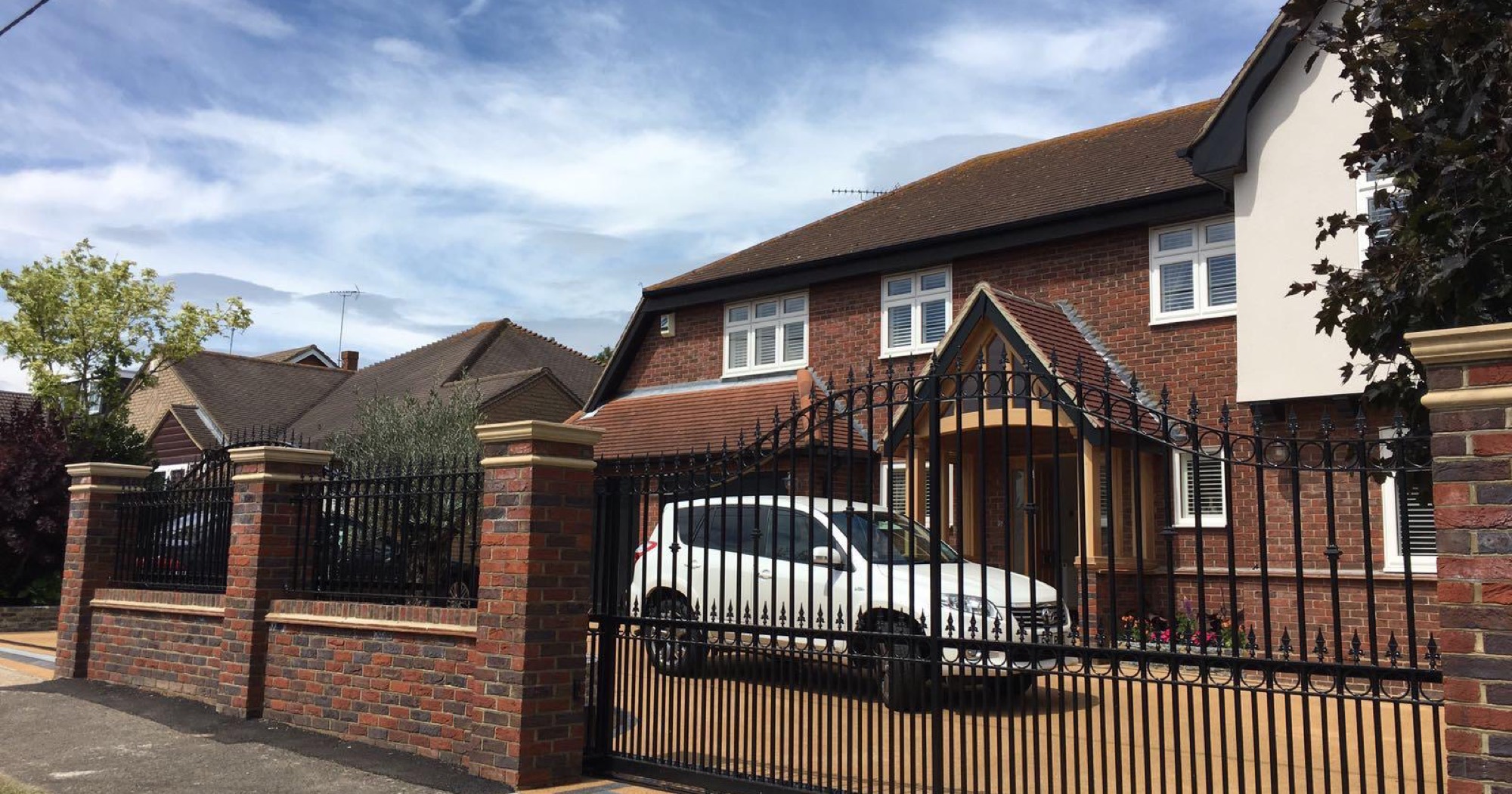 Detached house behind wrought iron gates hung on brick piers
