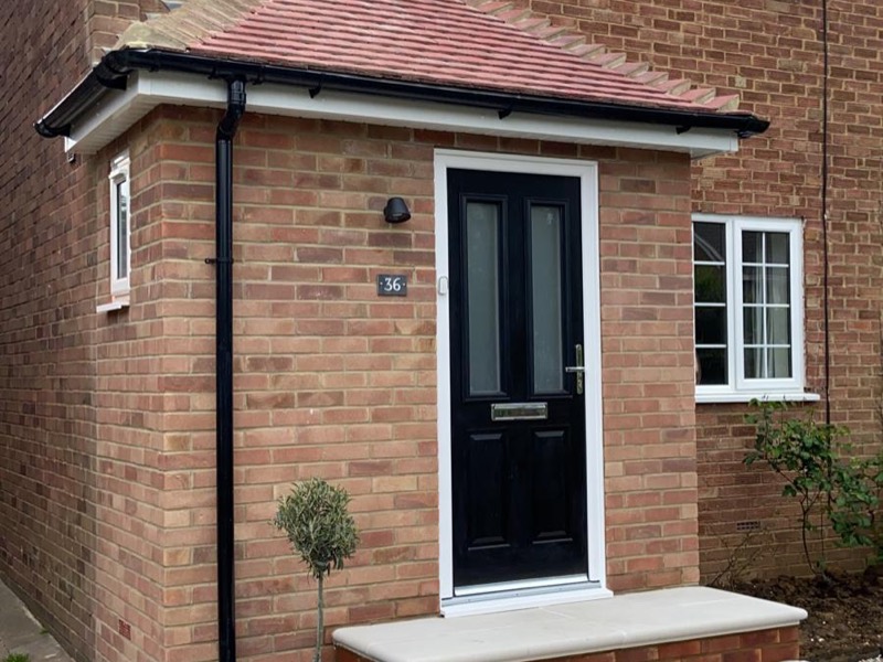 Red brick porch with a tiled roof and black door