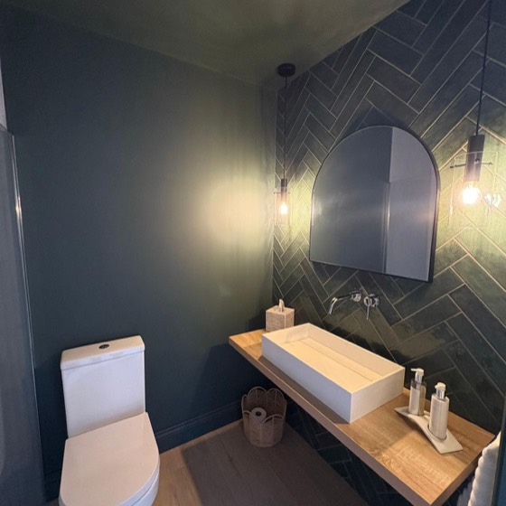 Green herringbone tiles, an arched mirror and an oak shelf