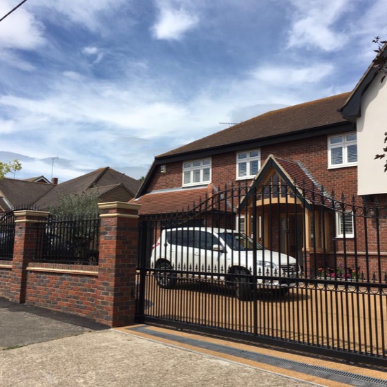 Wrought iron gates between brick piers in front of a detached house