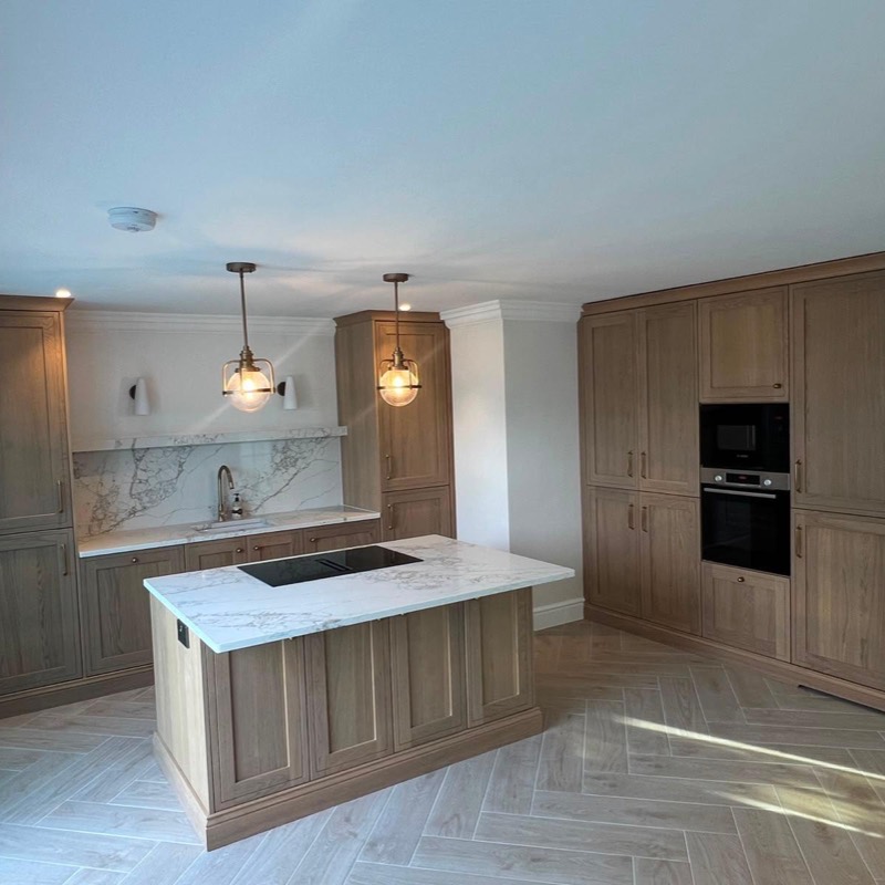 Oak shaker kitchen with a hob island, marble-effect worktops and brass pendant lights