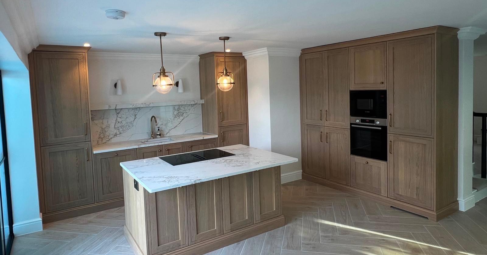 Oak shaker kitchen with a hob island, marble-effect worktops and brass pendant lights