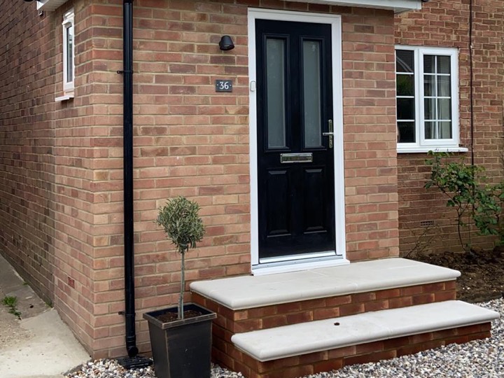 Red brick porch with a tiled roof, black front door and stone steps