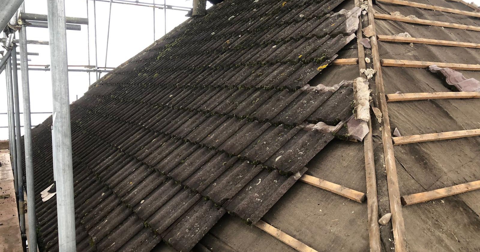 Old concrete roof tiles being stripped back to the battens under a scaffold roof