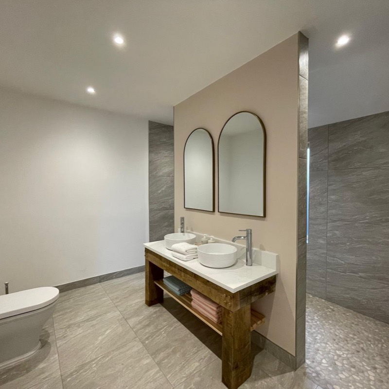 Double vanity on a rustic timber washstand, with arched mirrors and a walk-in shower behind