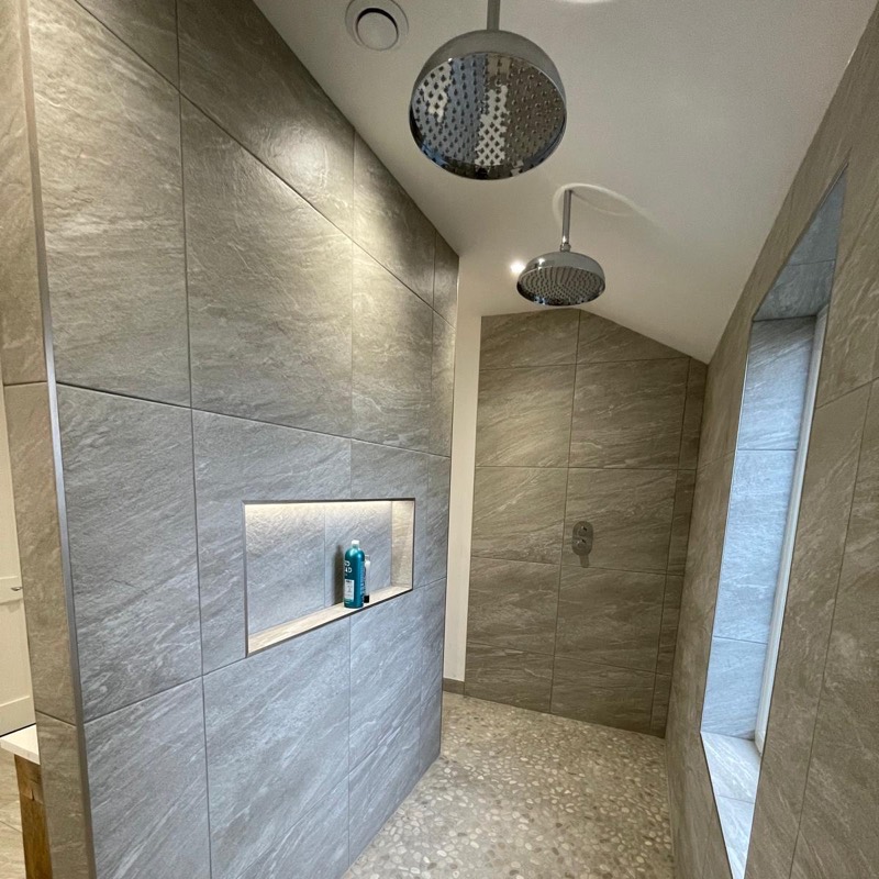 Walk-in shower with twin rain heads, a lit niche and a pebble floor