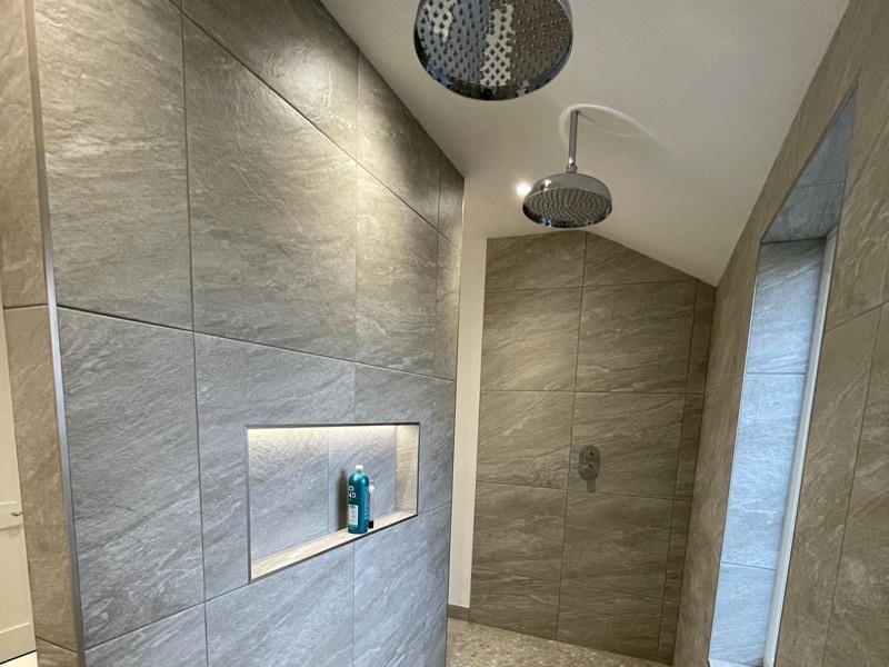 Walk-in shower with twin rain heads, large format tiles and a lit niche